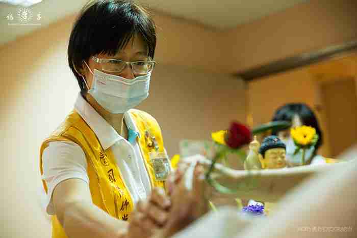佛光會西屯分會林淑玲會長在浴佛儀式後，遞上平安符、大悲水和鮮花與病友結緣