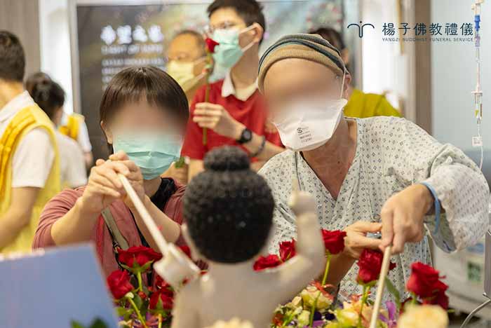 為了讓無法下床的病友也能親自參與，義工細心地將行動浴佛車推至床邊。病友與家屬舀起一杓淨水灌沐如來，這一刻的畫面，展現了生命在脆弱中依然保有的尊嚴。 ｜楊子佛教禮儀公司